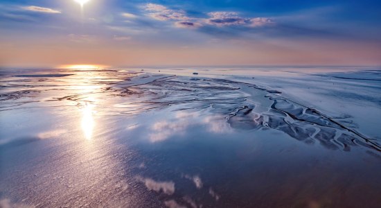 Luftaufnahme: Wolken und Sonne spiegeln sich eindrucksvoll im Wattenmeer vor Cuxhaven, © Martin Elsen