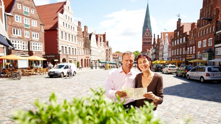 Zwei Menschen schauen auf einen Stadtplan, im Hintergrund ist der Platz Am Sande zu sehen., © Lüneburger Heide GmbH / Christian Wyrwa