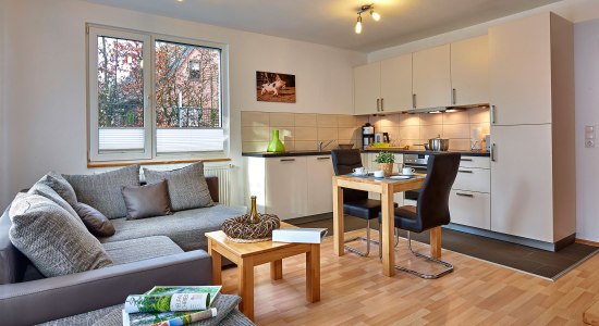 Einblick in den Wohnbereich mit grauem Sofa, kleinem Esstisch und Küche, © Tierpark Nordhorn gGmbH / Franz Frieling