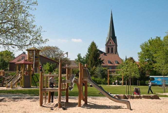 Spielgeräte auf einem Spielplatz. Im Hintergrund ist eine Kirche zu sehen, © LWT / Richard Heskamp