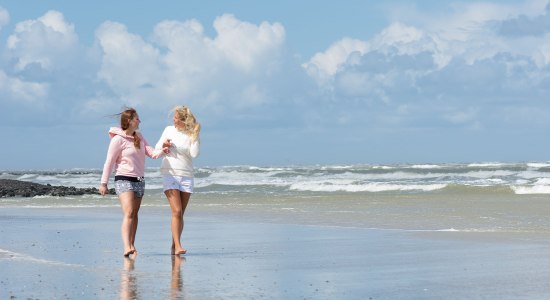 Zwei Frauen gehen mit den Füßen im Wasser am Strand entlang, © Kurverwaltung Wangerooge / Kees van Surksum