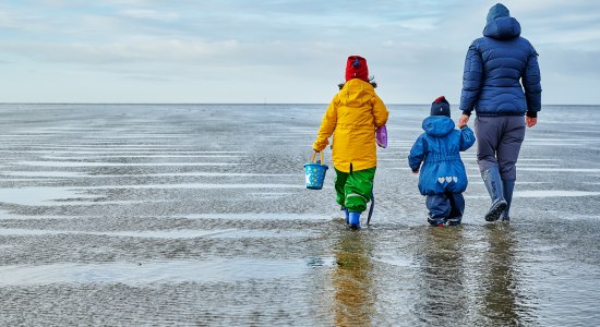 Frau geht mit Kindern im Watt spazieren.