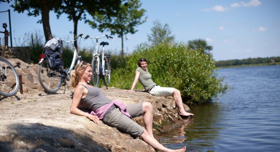 Radfahrerinnen sitzen an der Ems und halte ihre Füße ins Wasser., © Emsland Touristik GmbH