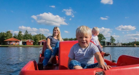 Eine Frau fährt mit ihren zwei Kindern mit einem roten Tretboot., © Südbrookmerland Touristik GmbH