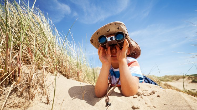 Junge liegt am Stand und schaut durch ein Fernglas, © Fotolia/ Brian Jackson