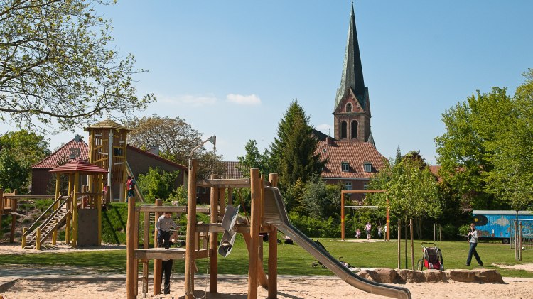 Spielgeräte auf einem Spielplatz. Im Hintergrund ist eine Kirche zu sehen, © LWT / Richard Heskamp